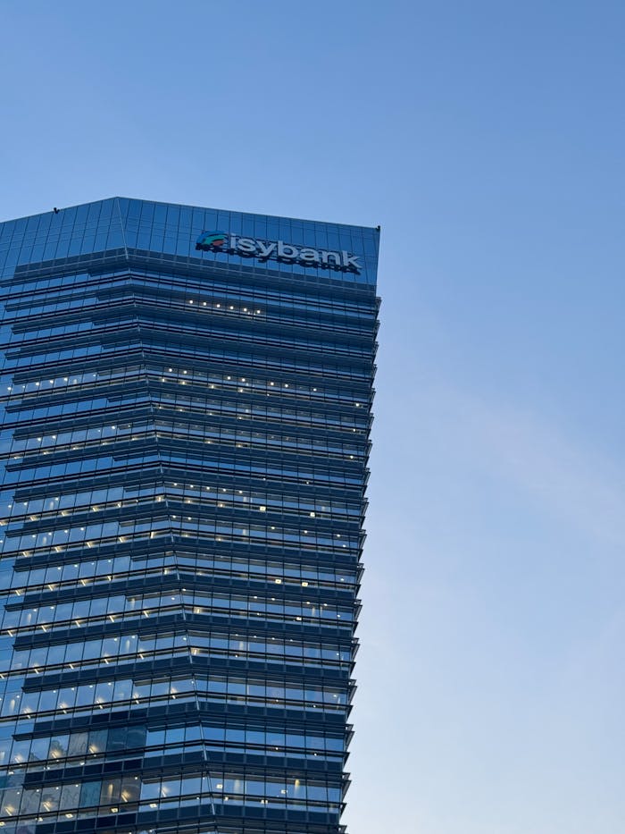 gallery-4 A tall glass skyscraper in Milan with Isybank logo against a clear blue sky.