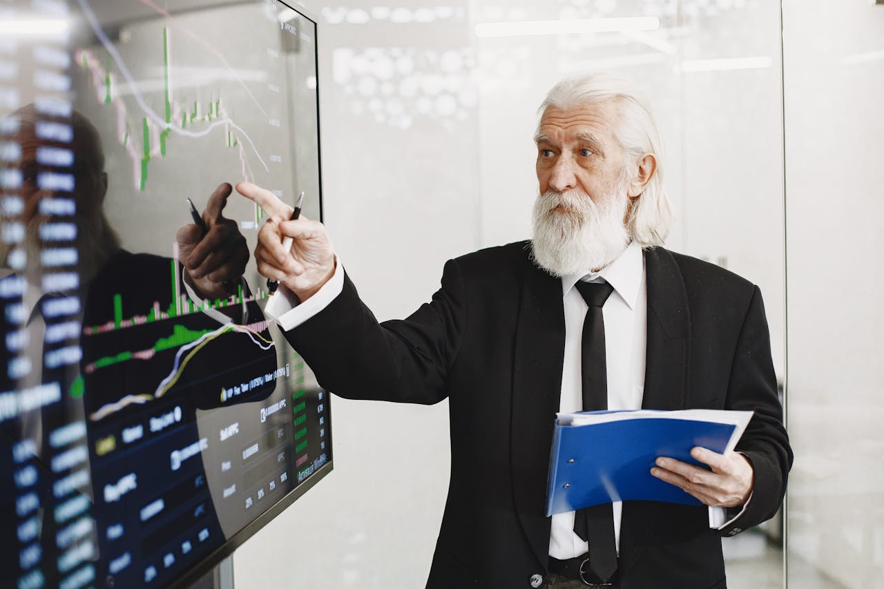 The Art of Drawing Readers In: Your attractive post title goes here Elderly businessman pointing at stock market charts in an office setting, highlighting data analysis.